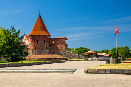 Medieval gothic Kaunas Castle with tower with red tiled roofs, red flag nearby and blue sky on background, Lithuaniaのeditorial素材