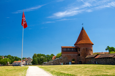 Medieval gothic Kaunas Castle with tower with red tiled roofs, red flag nearby and blue sky on background, Lithuaniaのeditorial素材