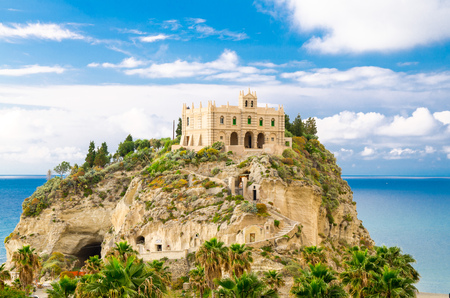 Monastery Sanctuary church Santa Maria dell Isola on top of rock of Tyrrhenian Sea and green palm trees, blue sky with white clouds around in sunny day, Tropea, Vibo Valentia, Calabria, Southern Italyの写真素材