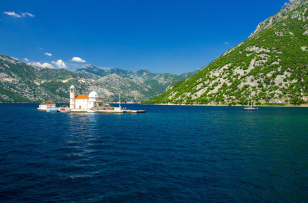 Roman Catholic Church Our Lady of the Rocks on island islet in Boka Kotor bay near Perast town in front of mountains range and blue sky with white clouds, Montenegroの写真素材