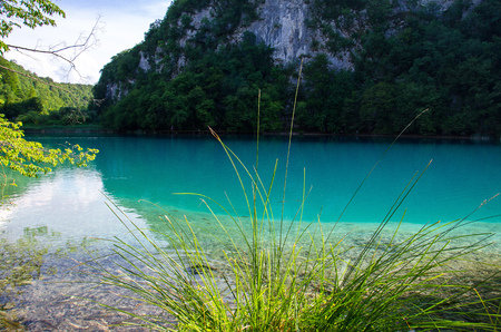 Beautiful view of lake with clear turquoise water, green plants trees and mountains rocks in the background, National park Plitvice Lakes, Croatia, Europeの写真素材