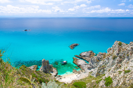 Aerial panoramic view of horizon and amazing tropical blue azure turquoise water of sea, rock cliff grass hill, yacht boat, blue sky background, Capo Vaticano, Calabria, Southern Italyの写真素材