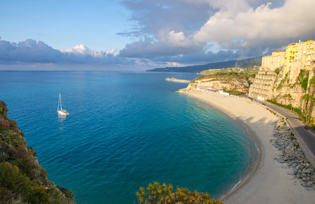 Tropea town and beach, yacht boat in Tyrrhenian Sea, colorful buildings on top of high big rocks,...