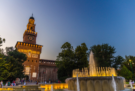 Old medieval Sforza Castle Castello Sforzesco facade, walls and tower La torre del Filarete with lights, trees, lighting fountain at sunset, dusk, twilight, evening, blue sky, Milan, Lombardy, Italyのeditorial素材