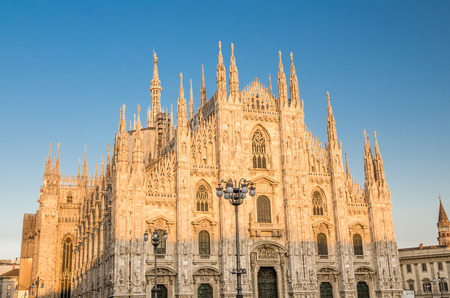 Duomo di Milano cathedral facade with white walls, high windows, spires, mouldings and stucco work, view from Piazza del Duomo square with blue sky background, Milan historical city centre, Italyの写真素材