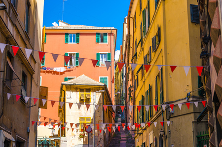 Small red and white flags hang above street with colorful multicolored buildings with shutters on windows in historical centre of old european city Genoa (Genova), Liguria, Italyの写真素材