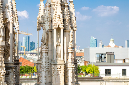 White marble statues figures on roof of famous Duomo di Milano Cathedral and top aerial view of Milan city centre skyscrapers with blue sky white clouds, Lombardy, Italyの写真素材