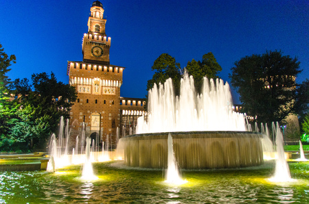 Old medieval Sforza Castle Castello Sforzesco facade, walls and tower La torre del Filarete with lights, trees, lighting fountain at sunset, dusk, twilight, evening, blue sky, Milan, Lombardy, Italyのeditorial素材