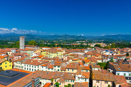 Aerial top panoramic view of Piazza dell Anfiteatro square, Chiesa di San Frediano church in historical centre medieval town Lucca with terracotta tiled roofs, green hills background, Tuscany, Italyの写真素材
