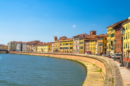 Row of old colorful buildings houses on embankment promenade of Arno river in historical centre of Pisa town with blue sky white clouds copy space background in sunny day, Tuscany, Italyの写真素材