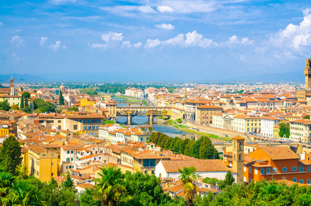 Top aerial panoramic view of Florence city with Ponte Vecchio bridge over Arno river, buildings with orange red tiled roofs, palm trees, blue sky white clouds, Tuscany, Italyの写真素材