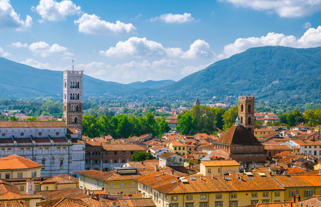 Aerial top panoramic view of Duomo di San Martino San Martin cathedral bell tower in historical centre medieval town Lucca with terracotta tiled roofs and mountain range background, Tuscany, Italyの写真素材