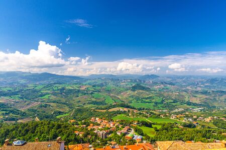 Aerial top panoramic view of landscape with valley, green hills, fields and villages of Republic San Marino suburban district with blue sky white clouds background. View from San Marino fortressの写真素材