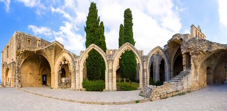Ancient ruins of the Bellapais Abbey monastery Bellabais ManastÄ±rÄ± in Kyrenia Girne with stone arches and thujas, blue sky white clouds background, Northern Cyprusの写真素材