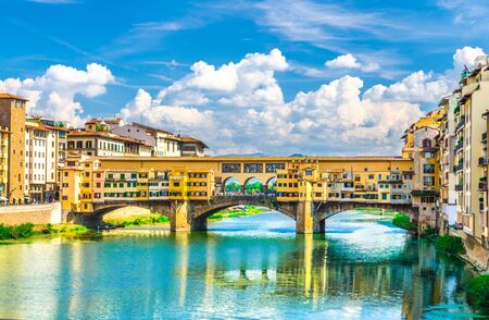 Ponte Vecchio stone bridge with colourful buildings houses over Arno River blue turquoise water and embankment promenade in historical centre of Florence city, blue sky white clouds, Tuscany, Italyの写真素材