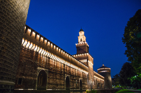 Old medieval Sforza Castle Castello Sforzesco lightning facade, walls, tower La torre del Filarete with lights, trees at sunset, dusk, twilight, evening, blue sky background, Milan, Lombardy, Italyのeditorial素材