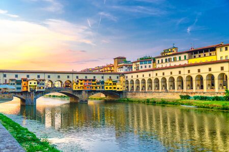 Ponte Vecchio bridge with colourful buildings houses over Arno River reflecting water and embankment promenade archways, historical centre of Florence city, blue evening sky clouds, Tuscany, Italyの写真素材