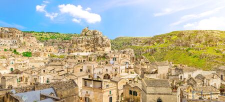 Rock church Santa Maria De Idris with big cross in historical centre of old ancient town Sassi di Matera in front of caves di Murgia Timone and dramatic sky, Basilicata, Southern Italyの写真素材