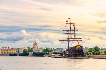 Cityscape of Saint Petersburg Leningrad with bascule Exchange Bridge, sailboat wooden ship with mast moored anchored on water of Neva river, evening dramatic orange sky background, Russiaの写真素材