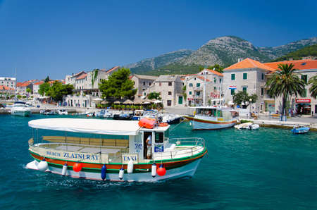 Brac, Croatia - May 17, 2016: Colourful Taxi boat in water of Marina Bol port of Pain in front of olt town and mountain hills, Brac Islandのeditorial素材