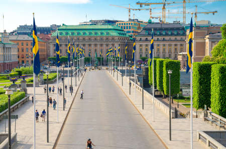 Sweden, Stockholm, May 29, 2018: Riksplan green grass lawn, bushes and street with national flags on Sodermalm island, Gustav Adolfs torg, Royal Swedish Opera house, blue sky with yellow cranesのeditorial素材