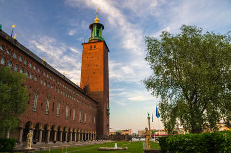 Sweden, Stockholm, May 29, 2018: City Hall Stadshuset tower building of Municipal Council and Nobel Prize on Kungsholmen Island in old town with blue sky, white clouds, Stadshusparken green treeのeditorial素材