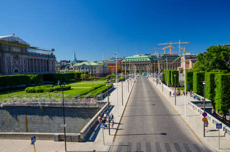 Sweden, Stockholm, May 31, 2018: Riksplan green grass lawn, bushes and street with national flags on Sodermalm island, Gustav Adolfs torg, Royal Swedish Opera house, blue sky with yellow cranesのeditorial素材