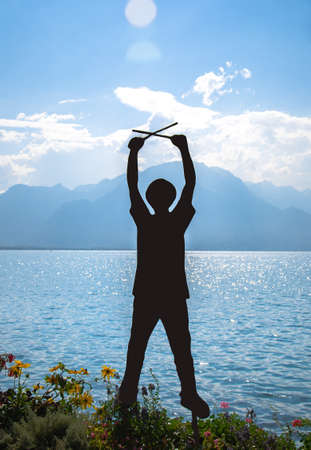 Montreux,  Switzerland - September 14, 2017: Figure silhouette of a man in a hat with drumsticks on promenade of the Lake Leman (Lake Geneva) in front of mountains Alps, Swiss Riviera, Vaud cantonのeditorial素材