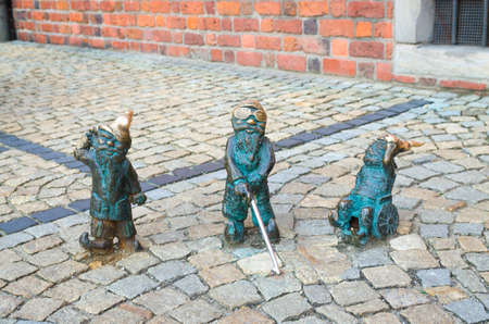 Wroclaw, Poland, May 7, 2019: three Dwarfs: deaf, blind with a stick and invalid in a wheelchair, famous bronze miniature gnome with hat sculpture is a symbol of Wroclaw in old historical city centreのeditorial素材