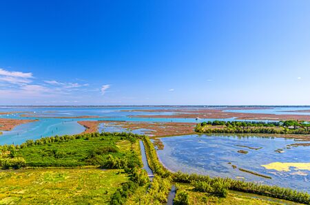 Aerial view of Torcello islands swamp, water canal and green trees and bushes. Panoramic view of Venetian Lagoon from bell tower. Veneto Region, Northern Italy. Blue cloudy sky background.の写真素材