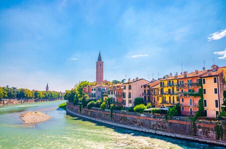 Verona cityscape with buildings on embankment of Adige river, bell tower Campanile di Santa Anastasia Catholic church, historical city centre, blue sky background, Veneto Region, Northern Italyの写真素材