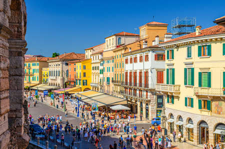 Verona, Italy, September 12, 2019: Row of old colorful multicolored buildings on Piazza Bra square in historical city centre, cafes and restaurants with tents and walking tourists, Veneto Regionのeditorial素材