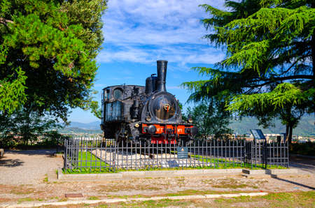 Brescia, Italy, September 11, 2019: Locomotiva a vapore SNFT - N.1 steam locomotive Prisoner monument on Cidneo Hill of Castle in green park, historical city centre, green trees blue sky, Lombardyのeditorial素材