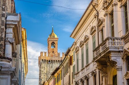 Top of Torre della Pallata brick medieval tower and old buildings with balconies and shutter windows, Brescia city historical centre, blue sky background, Lombardy, Northern Italyの写真素材