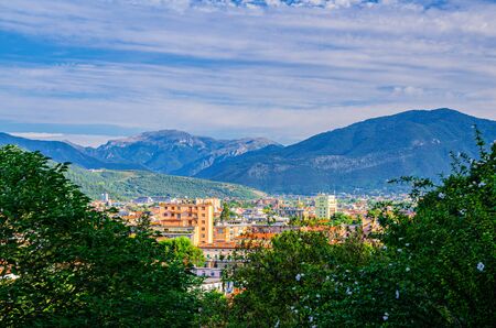 Aerial panoramic view of residential quarter of Brescia city and Alps mountain range, green trees foreground, blue cloudy sky, Lombardy, Northern Italyの写真素材