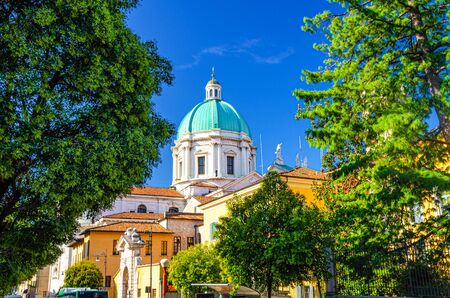 Santa Maria Assunta Roman Catholic church or New Cathedral or Duomo Nuovo building and green tree branches foreground, clear blue sky, Brescia city historical centre, Lombardy, Northern Italyの写真素材