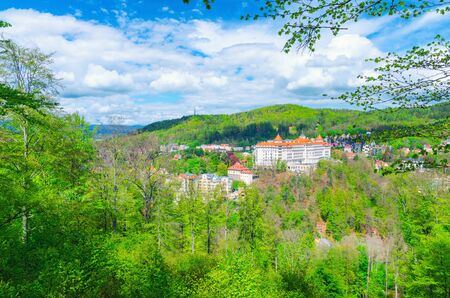 Karlovy Vary Carlsbad historical city centre top aerial view with hotels buildings, Slavkov Forest hills with green trees on slope, blue sky white clouds background, West Bohemia, Czech Republicの写真素材