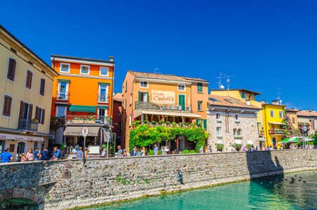 Sirmione, Italy, September 11, 2019: pedestrian street embankment in historical town centre with street restaurants and multicolored buildings with colorful walls, walking tourists, blue skyのeditorial素材