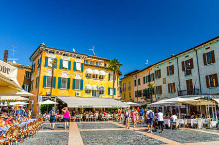 Sirmione, Italy, September 11, 2019: pedestrian street Piazza Giosue Carducci square in historical town centre with street restaurants and multicolored colorful buildings, walking tourists, blue skyのeditorial素材