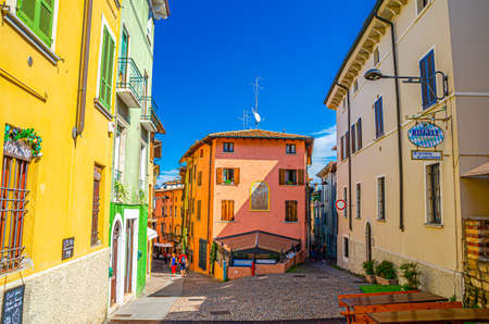 Desenzano del Garda, Italy, September 11, 2019: typical narrow street in old historical town centre with cobblestone road and traditional colorful buildings, blue sky background, Lombardyのeditorial素材
