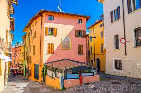 Desenzano del Garda, Italy, September 11, 2019: typical narrow street in old historical town centre with cobblestone road and traditional colorful buildings, blue sky background, Lombardyのeditorial素材