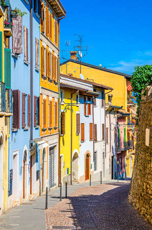 Typical narrow street in old historical centre of Desenzano del Garda town with cobblestone road and traditional colorful buildings with shutter windows, vertical view, Lombardy, Northern Italyの写真素材