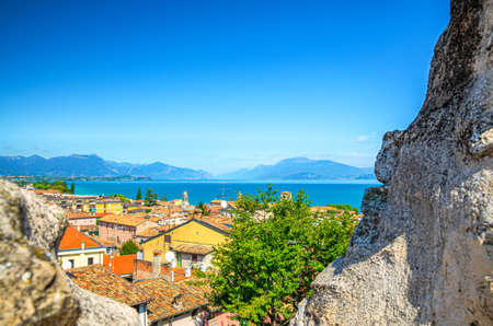 View of historical centre Desenzano del Garda old town, lake and mountain range through merlons of brick stone ruined wall of medieval castle, blue sky copy space, Lombardy, Northern Italyの写真素材
