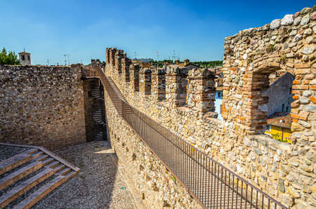 Desenzano del Garda, Italy, September 11, 2019: courtyard, spiral staircase and stone brick walls with merlons of medieval castle Castello di Desenzano, blue sky backgroundのeditorial素材
