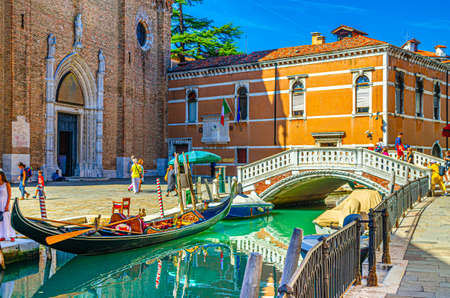 Venice, Italy, September 13, 2019: gondolas and boats moored on narrow water canal, Basilica di Santa Maria Gloriosa dei Frari catholic church and stone bridge, Veneto Region, blue sky in summer dayのeditorial素材