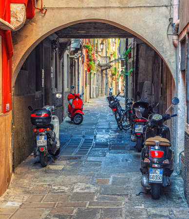 Chioggia, Italy, September 16, 2019: scooter motorbike Vespa and motorcycle in arch of narrow italian cobblestone street in historical town centre, Veneto Regionのeditorial素材