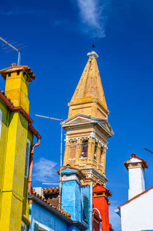 Roofs of colorful houses with multicolored walls and Bell tower of San Martino church in Burano island, blue bright sky in sunny summer day background, Venice Province, Veneto Region, Northern Italyの写真素材