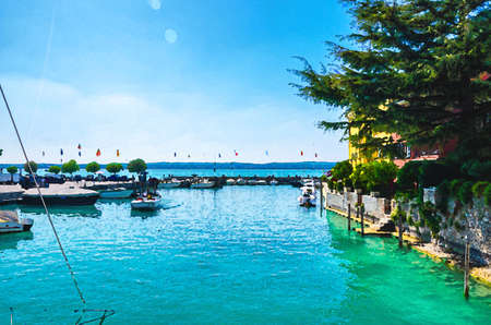 Watercolor drawing of Harbor of Garda lake with blue azure turquoise water, wooden pier dock and yacht, motor boats, coast and blue sky background, Sirmione town, Lombardy, Northern Italyの写真素材