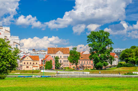 Traeckaje Suburb with old buildings in Trinity Hill district and grass lawn with green trees in Minsk city historical centre, blue sky white clouds in sunny summer day, Republic of Belarus