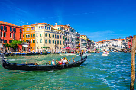 Venice, Italy, September 13, 2019: gondolier and tourists on gondola traditional boat sailing on water of Grand Canal with Venetian architecture typical colorful buildings and Rialto Bridge backgroundのeditorial素材